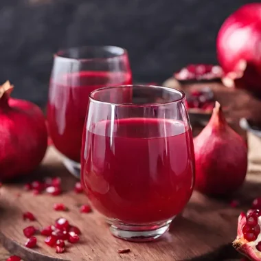 A glass of pomegranate juice surrounded by pomegranates.